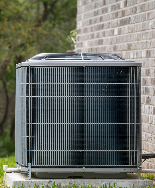 An outdoor air-conditioning condenser on a concrete pad beside a brick wall